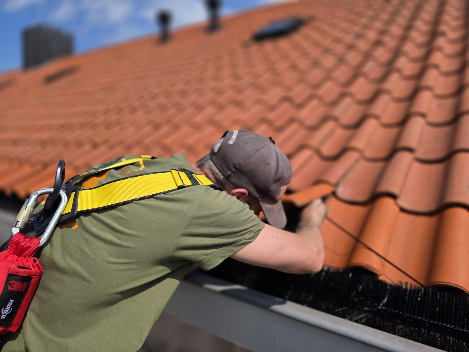 Medewerker met valbeveiliging inspecteert de dakrand van een pannendak