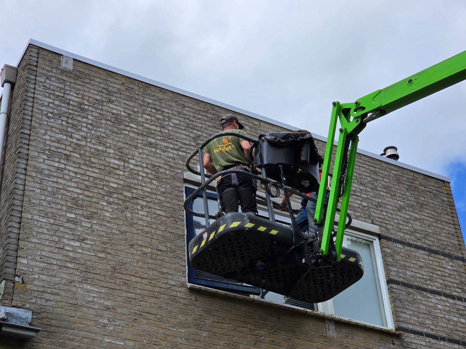 Medewerker van Habitat+ in een hoogwerker bij de dakrand van een woongebouw
