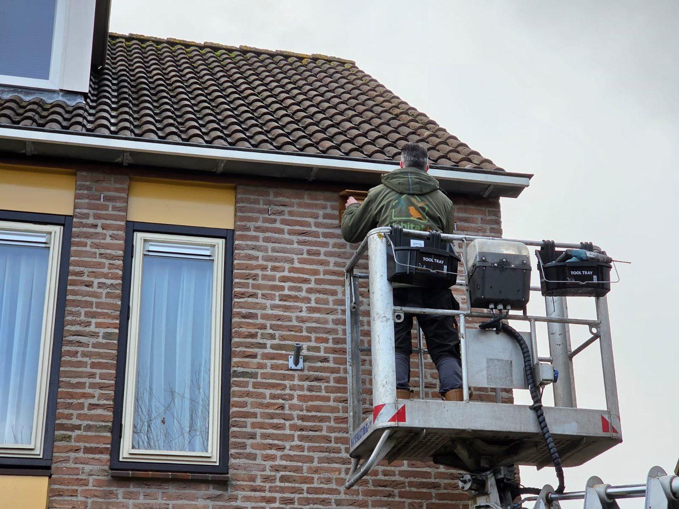 Medewerker in een hoogwerker inspecteert de dakrand van een woning