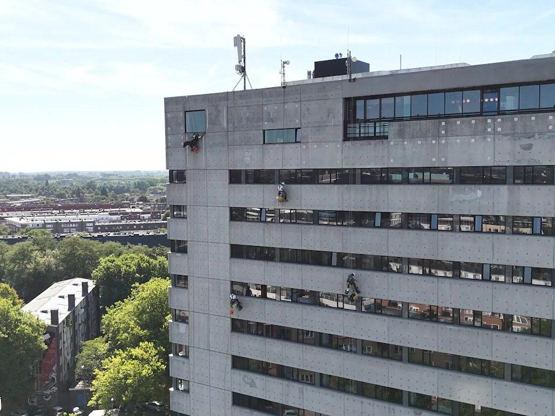 Vier medewerkers werken via touwtechniek langs de gevel van een hoog kantoorgebouw