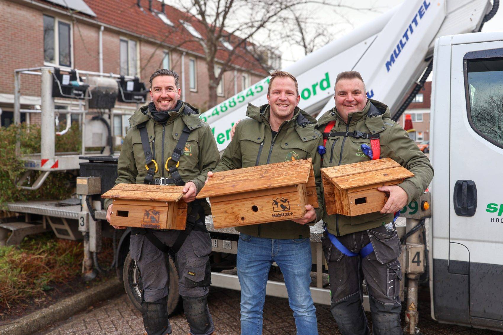 Drie medewerkers van Habitat+ met houten vleermuiskasten voor de hoogwerker